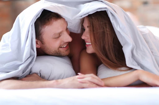 Muž a žena pod prikrývkou sa na seba usmievajú držiac sa za ruky