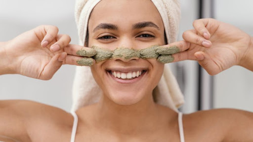 usmiata žena nanášajúca si prírodnú pleťovú masku na tvár